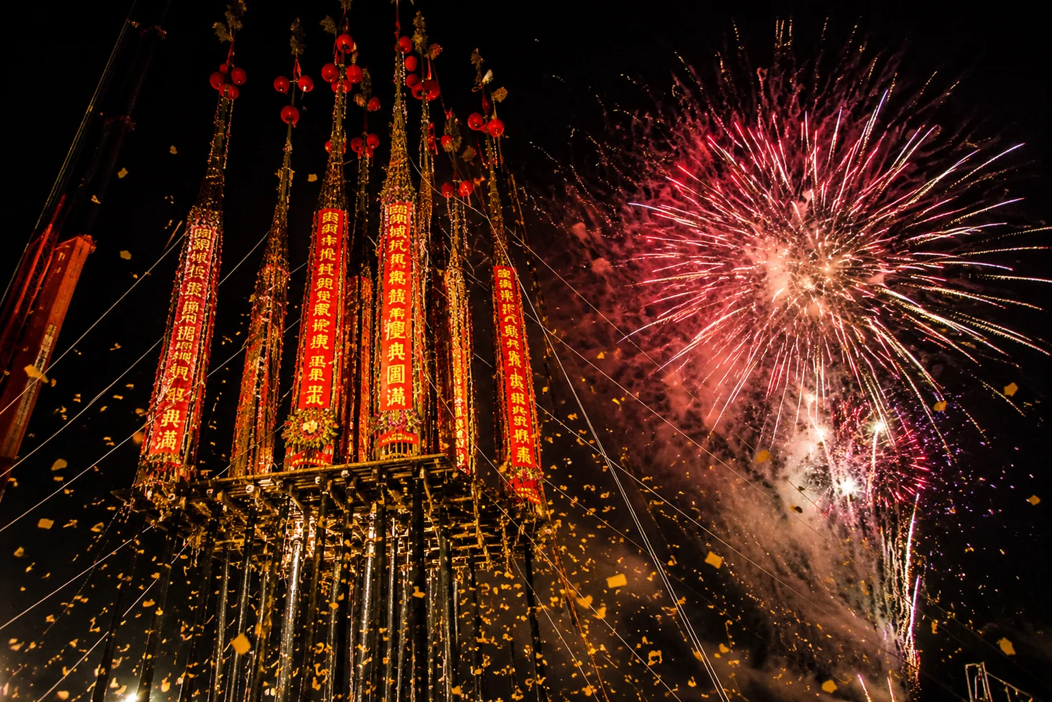 頭城搶孤孤棚立著多支高聳的孤棧與紅色布幔，夜空中煙火與碎紙屑同時飛舞
