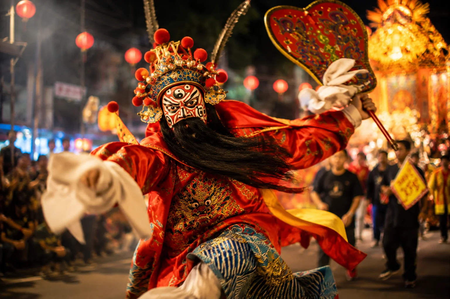 扮演鍾馗的陣頭演員臉譜化妝、身穿紅袍，在遊行隊伍中揮舞法扇，背後是燈火通明的花車與圍觀人群