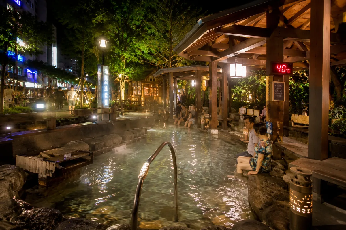夜晚的礁溪湯圍溝溫泉公園足湯池，木造涼亭下遊客坐在池邊泡腳，池畔立牌顯示水溫40度（示意圖，非現場實拍）