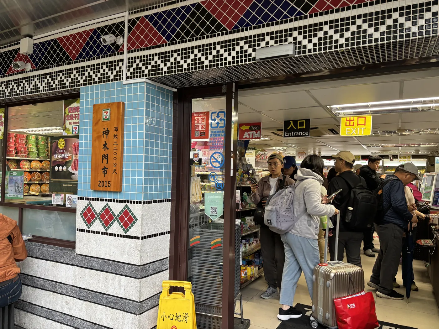 阿里山海拔 2200 公尺的 7-11 神木門市，門口掛著門市招牌，遊客拉著行李排隊結帳