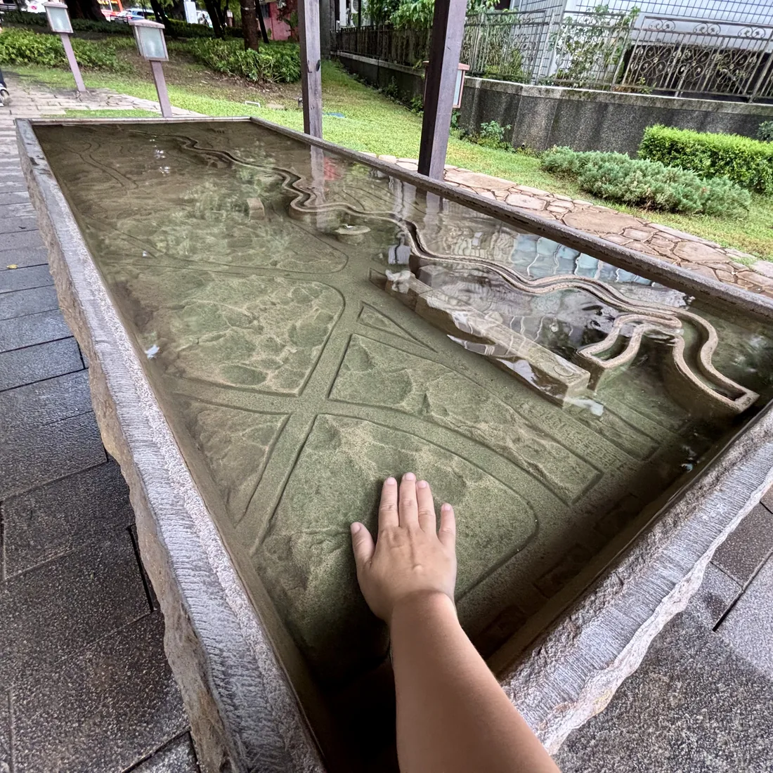 手掌伸進石造手湯池中，觸摸池底刻著北投地形的青磺泉溫泉水