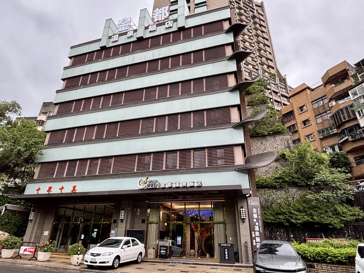 金都精緻溫泉飯店外觀，米綠色磚牆搭配深色窗框，招牌上寫著金都溫泉飯店字樣，門口停著白色轎車