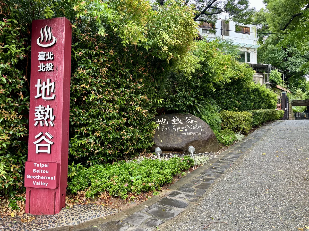 北投地熱谷入口的紅色立牌，中文與英文寫著地熱谷Hot Spring Valley，後方是茂密的綠色植栽