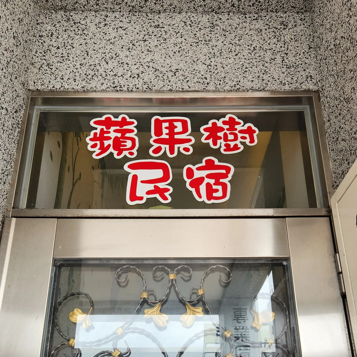 花蓮蘋果樹民宿玻璃門入口，紅色圓體字招牌與鑄鐵花紋玻璃門，門上貼著禁止吸菸標示
