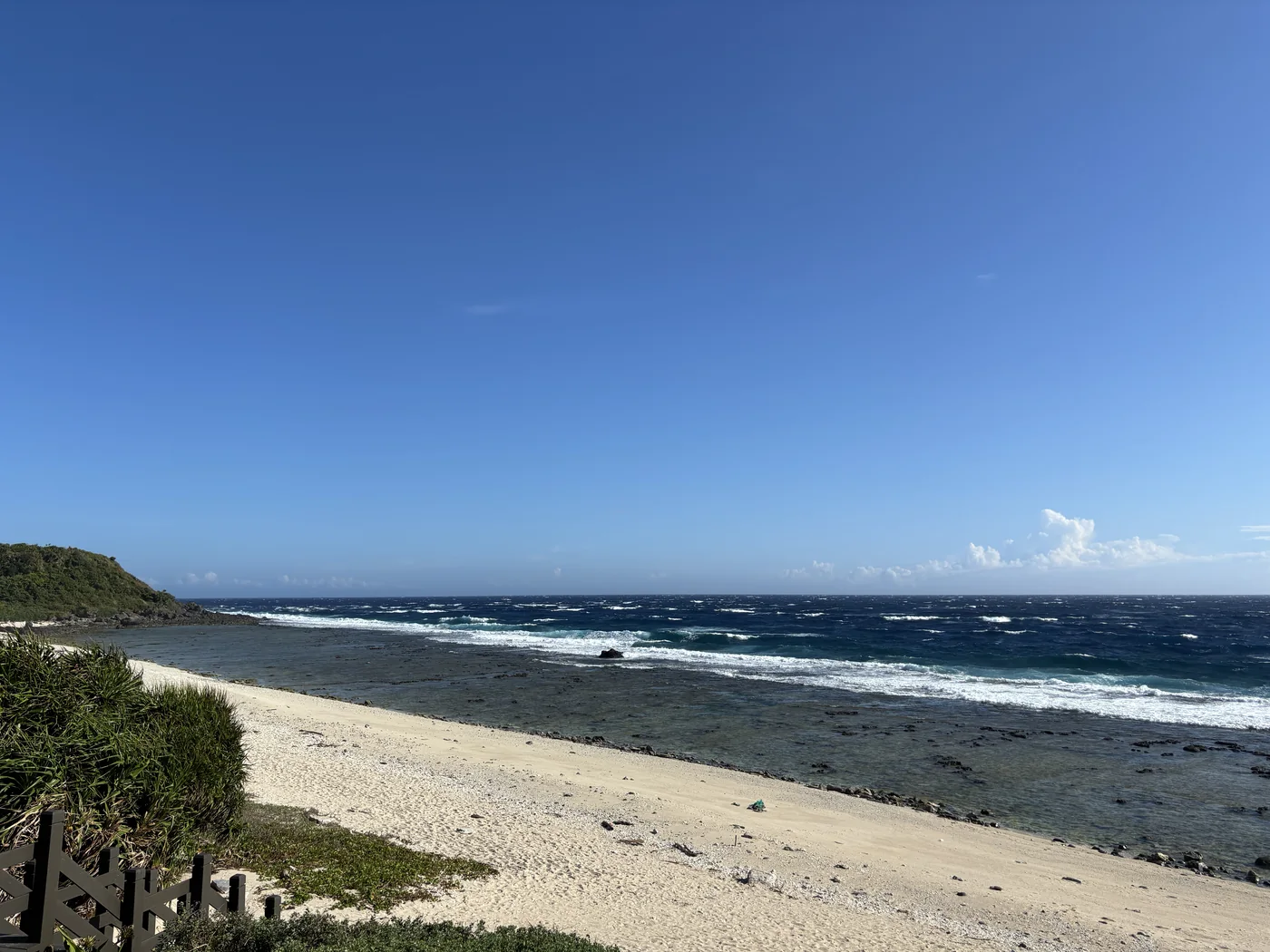 綠島海邊清澈的藍綠色海水與白沙灘，遠方是深藍的太平洋與礁岩