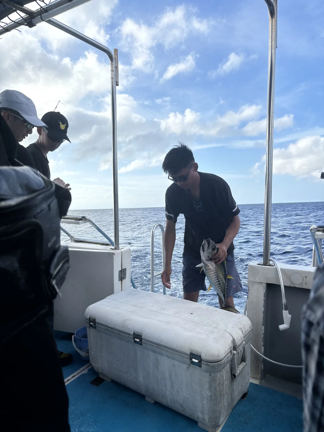 綠島外海的夜釣船上，一個人拿著剛拖釣上來的魚，旁邊是保冷冰箱與海面