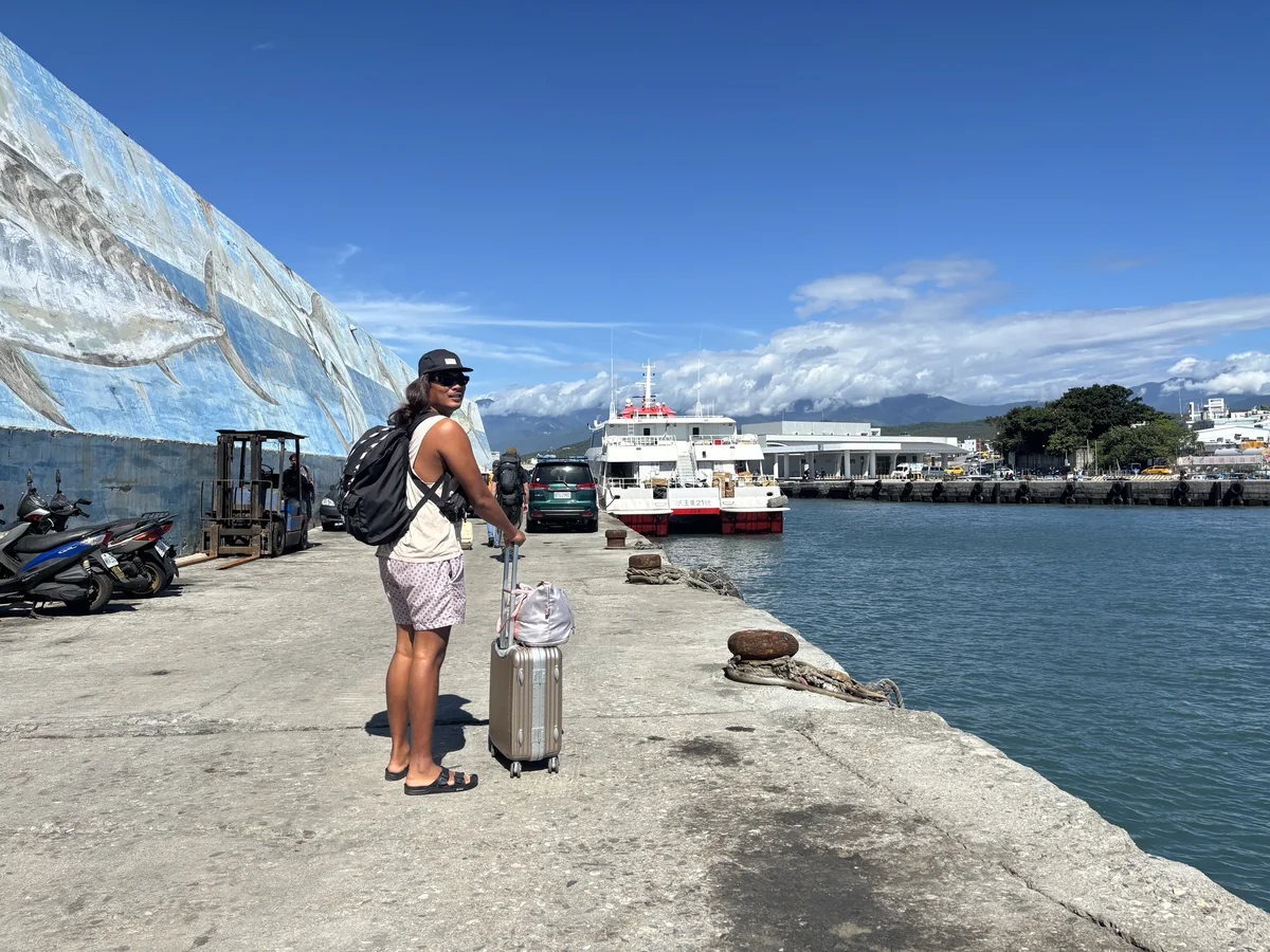 台東富岡漁港碼頭，旅客拉著行李等船，後方停著開往綠島的客船