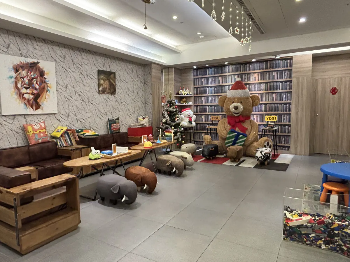 瑞德童話藝宿商旅大廳，巨大聖誕泰迪熊與樂高書牆裝飾，前方擺著動物造型椅凳