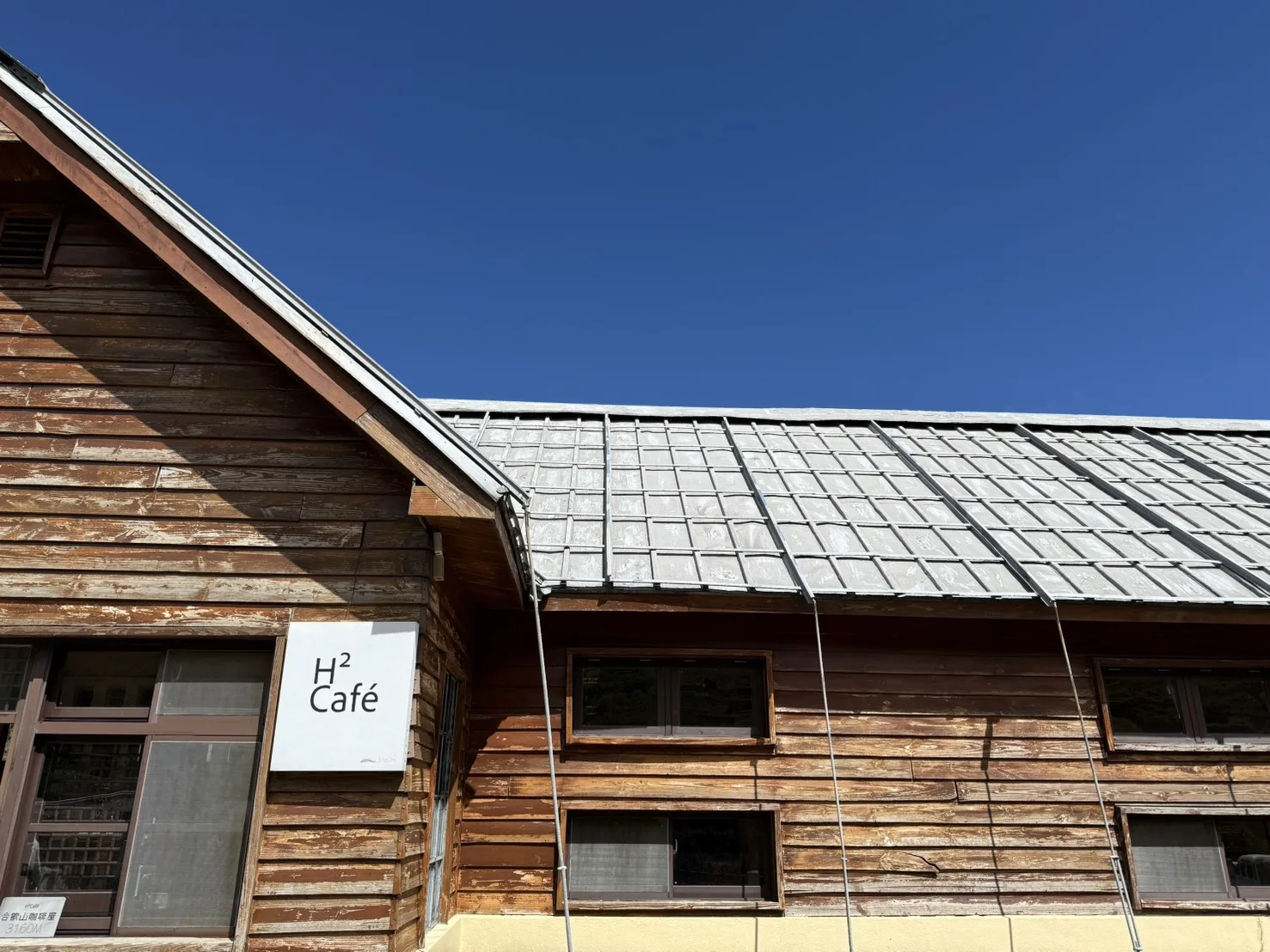 合歡山H2咖啡屋木造建築外觀，招牌標示海拔3160公尺，背景是藍天