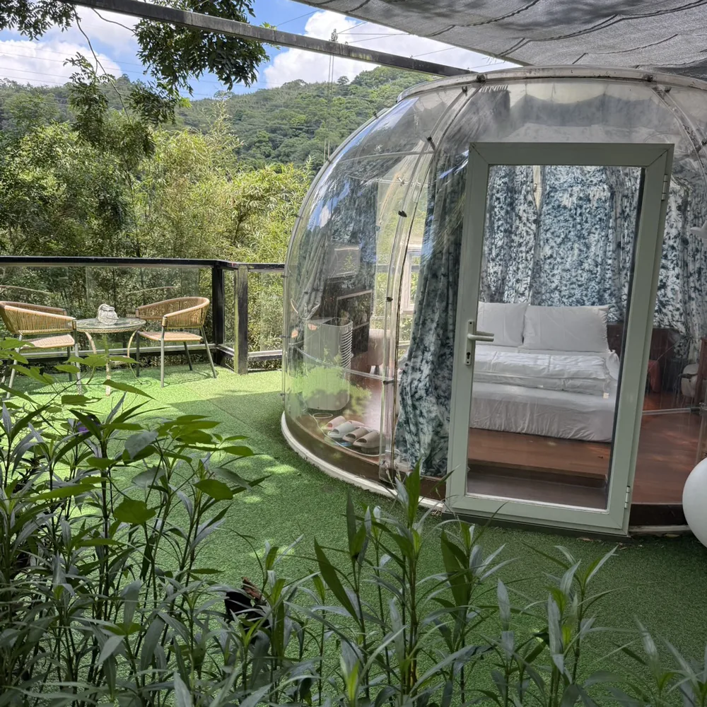 卓也小屋的透明泡泡屋客房，圓弧透明罩裡放著一張雙人床，外面是草地與竹林、遠處是山