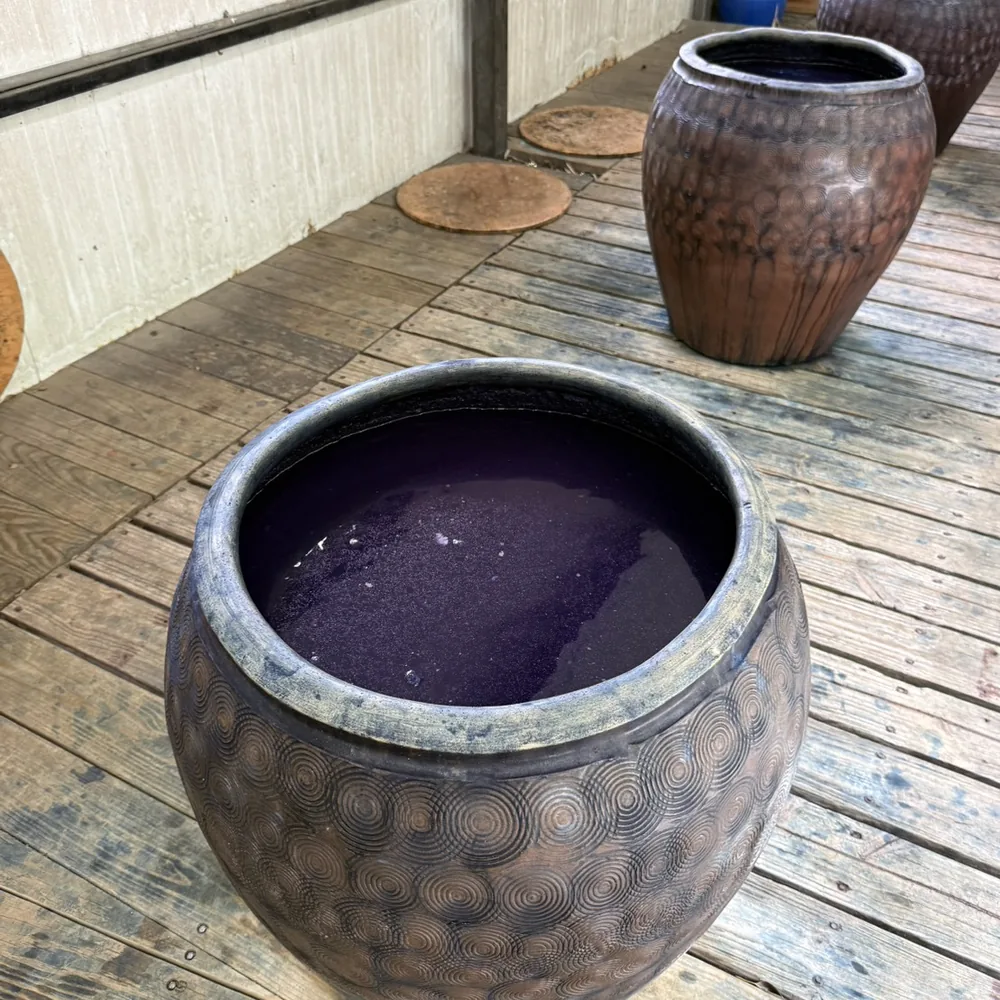 卓也小屋戶外木棧板上的陶製藍染缸，缸裡是深紫色的染液，旁邊還有幾個空的陶缸與木蓋