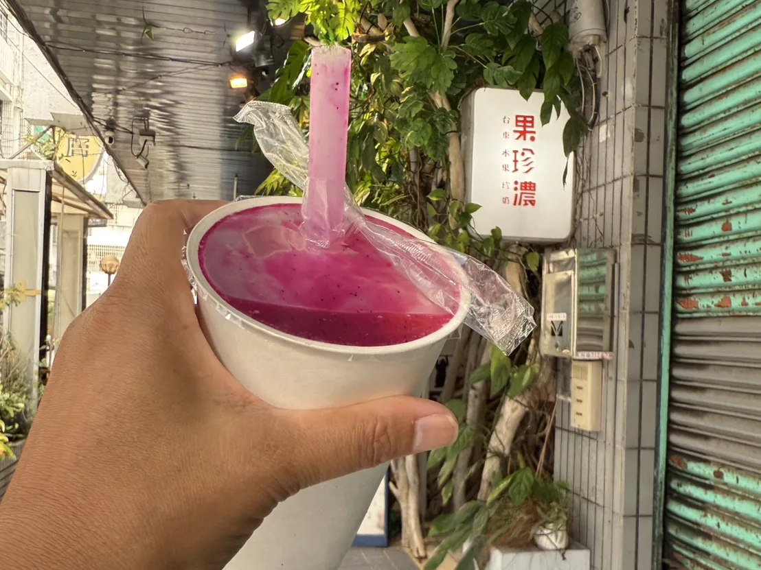 太麻里果珍濃現打火龍果汁，紫紅色飲料裝在紙杯中，背景是店家招牌