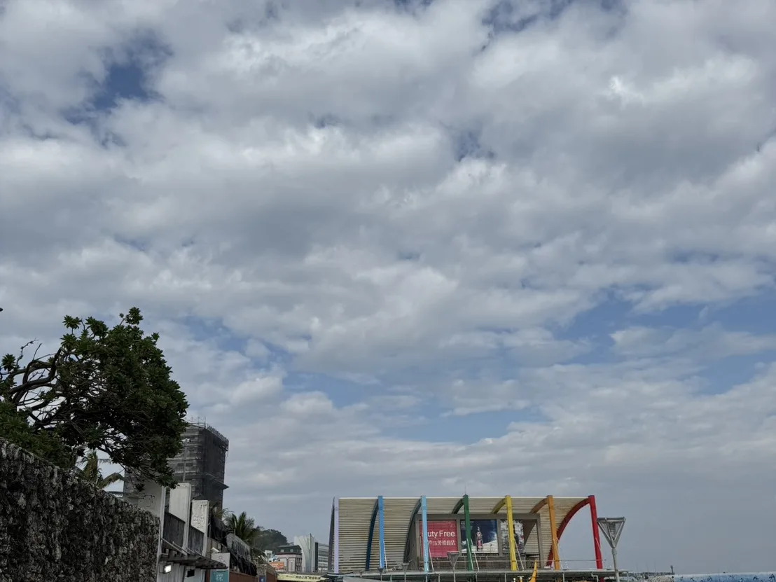 東港碼頭邊拖著行李箱準備搭船到小琉球的旅客，後方停靠著橘黃色雙體客船