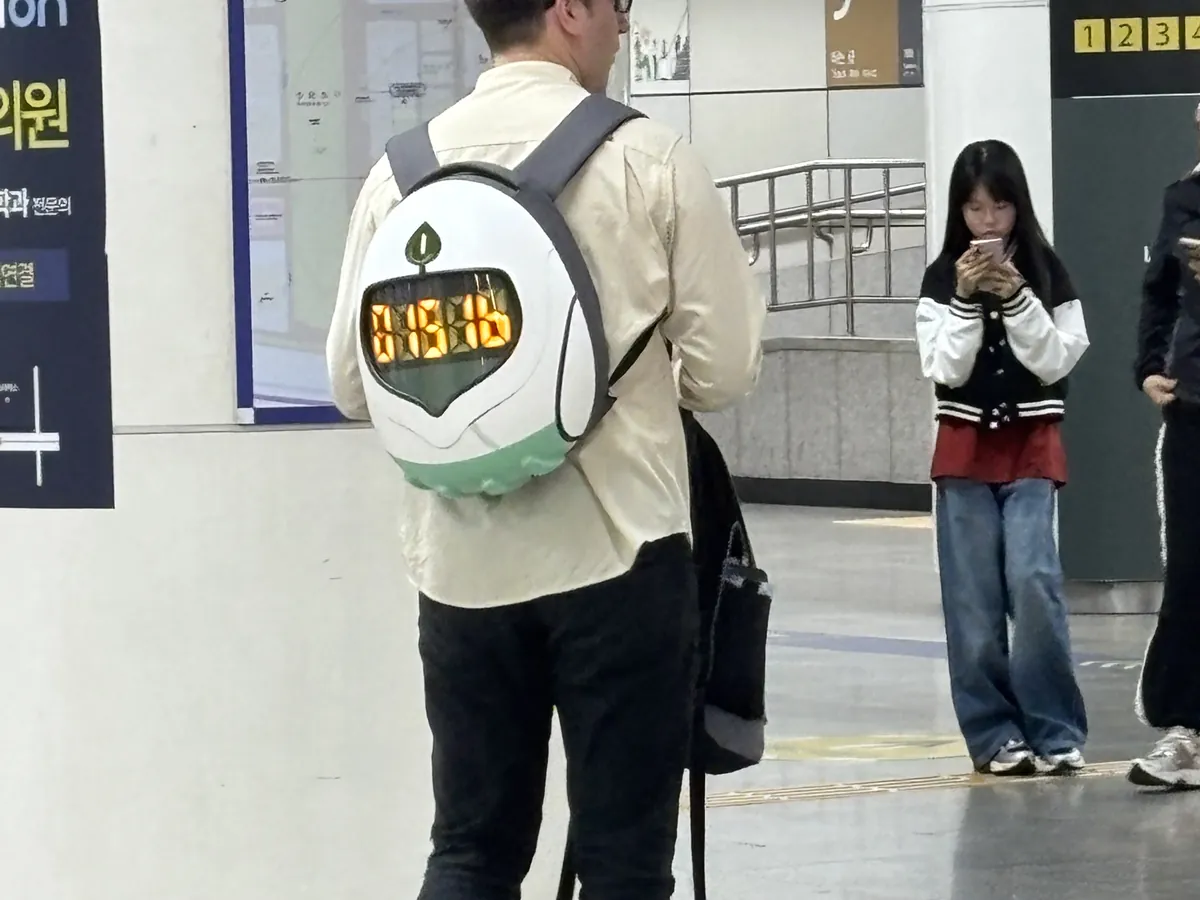 首爾地鐵站內背著3D列印客製皮克敏造型背包的乘客，背包正面有會發光的橘色顯示窗