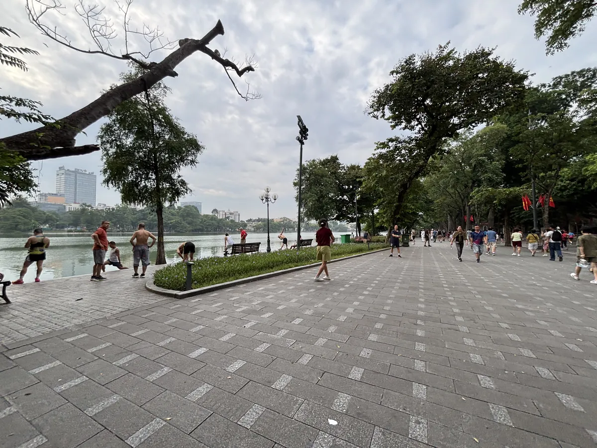河內還劍湖旁的步道，樹蔭下有當地人與旅客走動