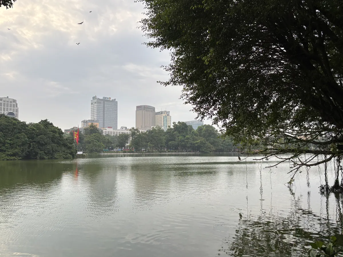 河內還劍湖的湖面與對岸樹林，湖邊有人散步