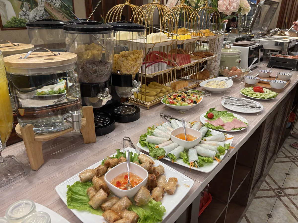 飯店早餐自助區，長桌上擺著多種冷盤、生菜與飲料機